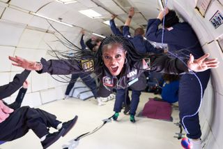 A woman floats in front of a large group during a parabolic flight of an airplane