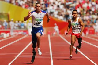 Two athletes sprint down a striped track with a large crowd behind them.