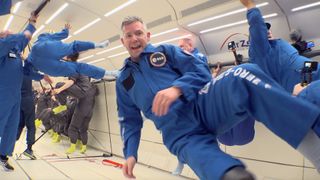 An astronaut in a flight suit floats in front of the camera during a parabolic flight.  Behind are many more astronauts in flight suits spinning in different directions